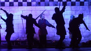 members of the Commonwealth Shakespeare Company rehearse a scene under blue stage lights from Shakespeare's Henry V in Bosto