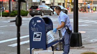 A United States Postal Service (USPS) worker wearing a protective mask and gloves makes his rounds in the Chelsea neighborhood of Manhattan as the city continues Phase 4 of re-opening following restrictions imposed to slow the spread of coronavirus on August 20, 2020 in New York City.