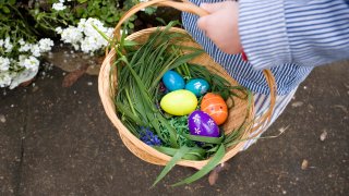 A child's hand holds a wicker basket containing plastic eggs.