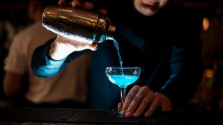 Bartender pours from a shaker into a glass of alcohol cocktail Blue Lagoon on a dark background