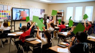 Students wearing protective masks raise their hands in a classroom as a teacher gives a lesson remotely at a public charter school in Provo, Utah, U.S., on Thursday, Aug. 20, 2020.