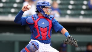 Cubs catcher PJ Higgins, wearing a blue helmet, blue and red chest protector, white pants and blue shin guards, throws a ball during a spring training game against Milwaukee