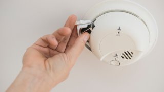 A person replaces the battery in a smoke detector.