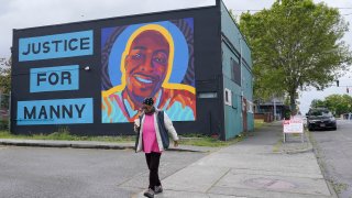 A woman walks past a mural honoring Manuel "Manny" Ellis, Thursday, May 27, 2021, in the Hilltop neighborhood of Tacoma, Wash., south of Seattle. Ellis died on March 3, 2020 after he was restrained by police officers. Earlier in the day Thursday, the Washington state attorney general filed criminal charges against three police officers in the death of Ellis, who told the Tacoma officers who were restraining him he couldn't breathe before he died.