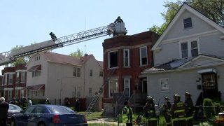 Chicago firefighters scale a ladder to reach the top of a red brick structure during a fire in the West Pullman neighborhood.