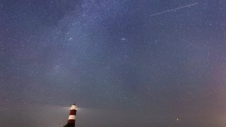 A meteor during the Perseid meteor shower seen over Happisburgh lighthouse, Norfolk, as the Earth flies through a cloud of cometary dust creating a spectacular display of celestial fireworks.