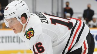 Blackhawks defenseman Nikita Zadorov stands on the ice during a game, wearing a white jersey, white helmet and black hockey pants