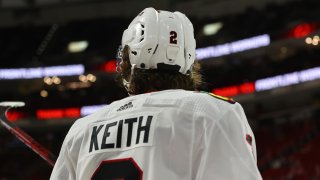 Blackhawks defenseman Duncan Keith, wearing a white jersey with black lettering and a white helmet, stands with his back to the camera during a game