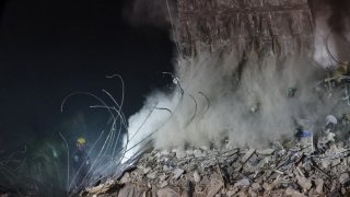 Search and rescue workers watch as rubble is carried by an excavator at the site of the collapsed 12-story Champlain Towers South condo building on July 09, 2021 in Surfside, Florida.