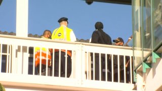 Two uniformed CTA personnel, both wearing yellow reflective jackets, and two Chicago police officers stand behind a railing at a Green Line station