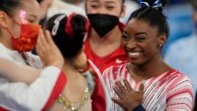 Simone Biles, of the United States, smiles as Tang Xijing, of China, left, embraces teammate Guan Chenchen after the latter won the gold medal