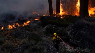 A firefighter carries a water hose toward a spot fire from the Caldor Fire burning along Highway 89 near South Lake Tahoe, Calif., Thursday, Sept. 2, 2021.
