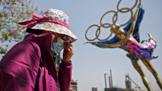 FILE - In this May 2, 2021, file photo, a woman adjusts her face mask as she walks by a statue featuring the Beijing Winter Olympics figure skating on display at the Shougang Park in Beijing. China's "zero tolerance" strategy of trying to isolate every case and stop transmission of the coronavirus has kept kept the country where the virus first was detected in late 2019 largely free of the disease.