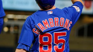 Cubs infielder Trent Giambrone, wearing a blue jersey and helmet wtih red lettering, points his finger to the sky after getting a base hit in his big league debut