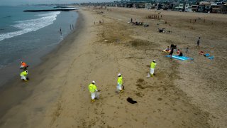 Workers in protective suits clean the contaminated beach