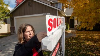 Real estate broker Rebecca Van Camp places a "Sold" placard on her sign in front of a home