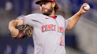 Reds pitcher Wade Miley, wearing a gray jersey with red lettering and a red baseball cap, throws a pitch during a game against the Miami Marlins