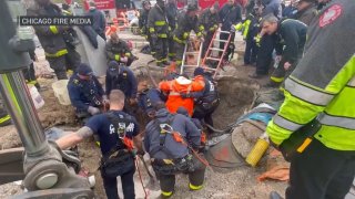 A large group of firefighters surround a worker who became trapped in a dirt and debris-filled hole in the South Shore neighborhood.