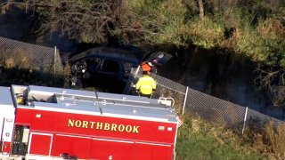 A black SUV remains partially submerged in a lagoon, while firefighters move around the scene