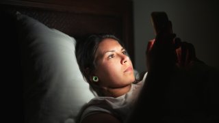 Young woman laying in bed and using smart phone at low light