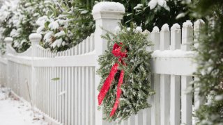 Christmas wreath hanging on white fence covered in snow