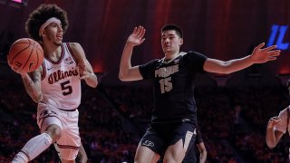 Illinois player Andre Curbelo, wearing a white jersey and white shorts, tries to throw the ball around Purdue center Zach Edey, wearing a black jersey with gold trim, during a game between the two teams on Jan. 17, 2022.