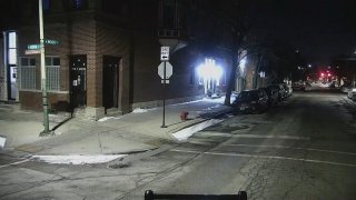 An intersection at night time in Chicago, with a brown, brick building in the background and several parked cars in the foreground