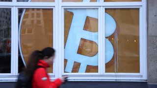 A young woman walks past a Bitcoin symbol in the window of a company that offers blockchain application services.