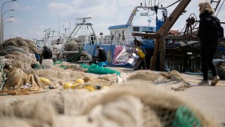 Fishermen mend nets in front of fishing boats at harbor in the Roman port of Fiumicino, Friday, March 11, 2022.