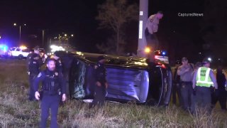 A black SUV lays on its side, with an Illinois State Police trooper standing on top of it, after a crash on the Bishop Ford Expressway in suburban Dolton