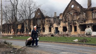 A woman pulls her bags past houses damaged during a fighting in Mariupol, on the territory which is now under the Government of the Donetsk People's Republic control, eastern in Mariupol, Ukraine, Friday, April 8, 2022.