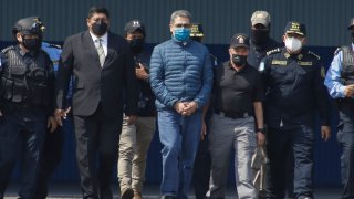 Former Honduran President Juan Orlando Hernandez, center, is taken in handcuffs to a waiting aircraft as he is extradited to the United States, at an Air Force base in Tegucigalpa, Honduras, Thursday, April 21, 2022. Honduras' Supreme Court approved the extradition of Hernandez to the United States to face drug trafficking and weapons charges.