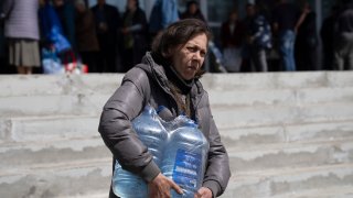 A woman carries bottles of drinking water from a distribution centre in Toretsk, eastern Ukraine, Monday, April 25, 2022. Toretsk residents have had no access to water for more than two months because of the war.