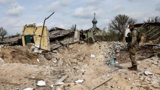 A Ukranian serviceman looks into a crater and a destroyed home in the village of Yatskivka, eastern Ukraine on April 16, 2022. Russia is making “incremental progress” in Donbas after little progress was made through its earlier two tactics, a senior U.S. defense official said in a briefing.
