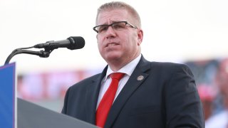 State Senator Darren Bailey, wearing a red tie and black jacket, speaks at an outdoor rally that also starred former President Donald Trump in June 2022