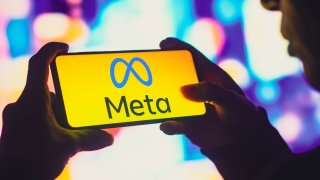 In this photo illustration, a silhouetted woman holds a smartphone with the Meta Platforms, Inc. logo displayed on the screen.