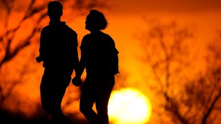 FILE - In this March 10, 2021 file photo, a couple walks through a park at sunset in Kansas City, Mo.