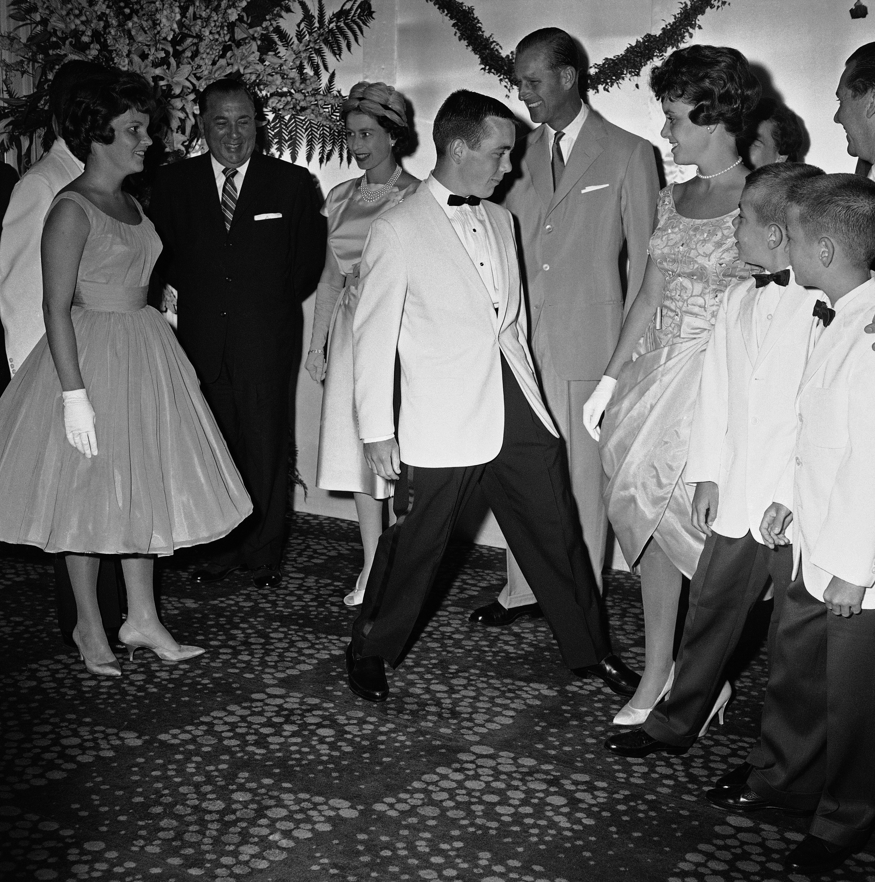 While adults enjoy the scene, sons and daughter of Mayor Richard Daley of Chicago, left, move into position to have their picture made with Queen Elizabeth II and Prince Philip, who seem willing enough, at reception for visiting royalty at Drake Hotel, July 6, 1959 in Chicago. (AP Photo/J.Walter Green)