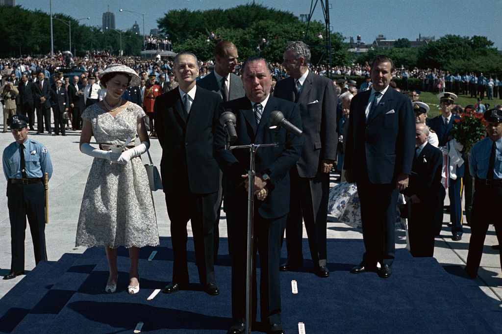 (Original Caption) Riding through the city in the motorcade, Queen Elizabeth waves to the thousands of spectators on her arrival here 7/6/59. In center is Illinois Governor William G. Stratton. Next to the Governor is Chicago’s Mayor Richard Daley. It is the Queen’s first major stop on U.S. soil in her current tour and her first visit to Chicago.