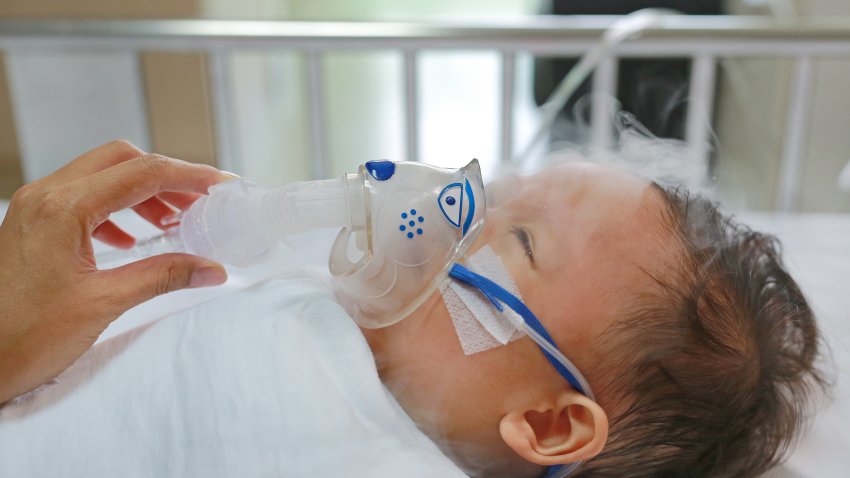 Toddler boy using nebulizer to cure asthma or pneumonia disease . Sick baby boy rest on patients bed and has inhalation therapy by the mask of inhaler. Respiratory Syncytial Virus (RSV).