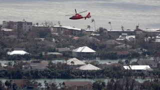 In this aerial view, a Coast Guard helicopter flies over the island as search and rescue efforts continue after Hurricane Ian