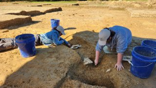 In this photo provided by John Crawmer, Jane C. Skinner and Samantha Muscella are excavating post holes at the bottom of the stockade trench.