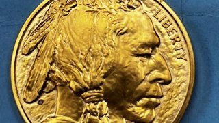 A gold coin, adorned with a Native American head facing toward the right, is pictured. The coin is an "American Buffalo" coin, valued at nearly $2,000