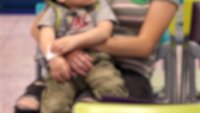 a blurred photo of a person holding a toddler on their lap. The toddler is wearing a hospital bracelet.