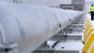 A worker walks past gas pipes that connect a Floating Storage and Regasification Unit ship with the main land in Wilhelmshaven, northern Germany on December 17, 2022. EU energy ministers are wrangling over a proposed price cap on gas.