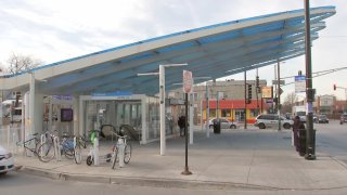 The CTA's Belmont station is pictured, with a blue and white steel roof spanning upward at a 45-degree angle above the entrance to the station, pictured at street level