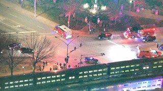 Two Metra trains, shown in the bottom of the image, remain on a train line near the intersection of two roads in Arlington Heights. A dark-colored SUV, which was struck by one of the trains, rests just to the north of the intersection