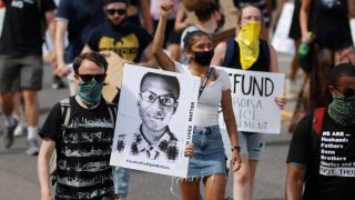 FILE – Demonstrators carry placards as they walk down Sable Boulevard during a rally and march over the death of Elijah McClain in Aurora, Colo., on June 27, 2020. A group of police officers and paramedics charged in the death of McClain, a 23-year-old Black man who was forcibly restrained and injected with a powerful sedative, are scheduled to appear in court Friday, Jan. 20, 2023, to enter pleas to the allegations.