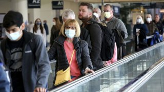 Air travelers, some with face masks and others without, use the moving walkway toward their gate at Midway International Airport in Chicago, Tuesday April 19, 2022. (Antonio Perez/Chicago Tribune/Tribune News Service via Getty Images)