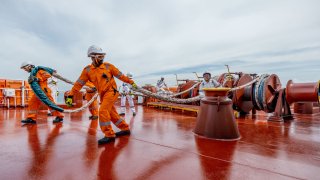 Oil tanker crew prepare mooring ropes to secure a bunker barge to their vessel for refueling.